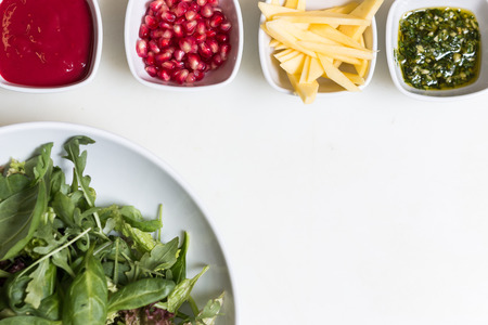 Arugula salad with pomegranate seeds and sauce, pesto sauce and freshly cut avocado in bowls on white backgroundの写真素材
