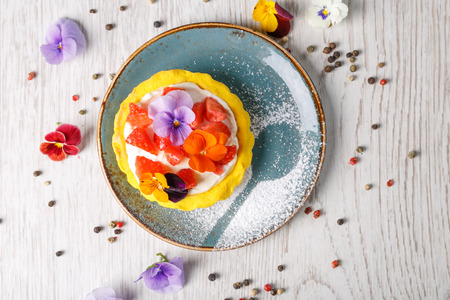 Strawberry tart garnished with edible flowers on a blue plateの写真素材