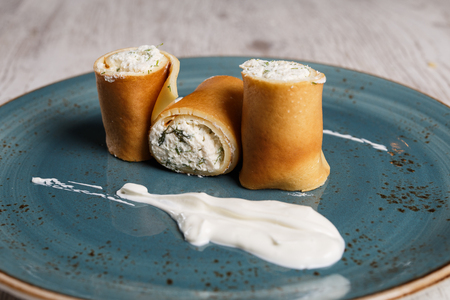 European pancakes, crepes, with cream cheese and sour cream on a blue plateの写真素材