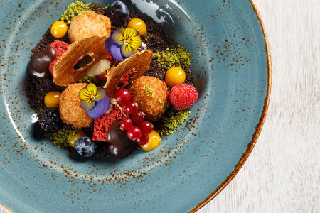Dried apples with ground pistachios, garnished with forest fruits and molten chocolate on a blue plateの写真素材