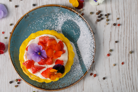 Strawberry tart garnished with edible flowers on a blue plateの写真素材