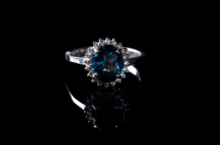 Silver ring with blue topaz isolated on a black background. Luxury jewelry closeup.の写真素材
