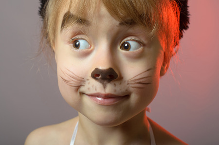 Portrait of a little girl with cat make-up on a gray background. Beautiful girl in carnival costume.の写真素材