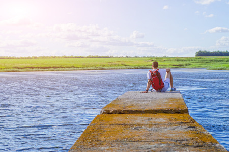A man sits on a river pier and looks at the sunset, free space. The tourist sits on the fishing bridge.の写真素材