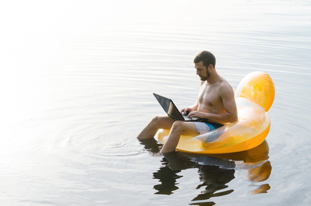 A man with a laptop on an inflatable ring in the water at sunset, free space. Businessman is resting on the sea.の写真素材