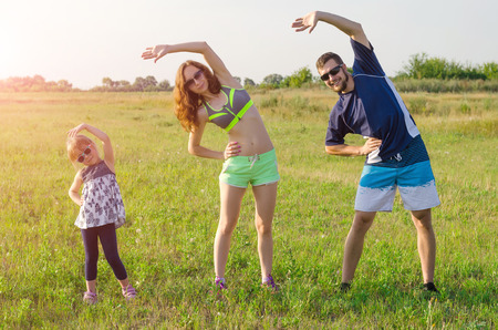 Happy young family doing exercises outdoors. Mom, Dad and daughter, sports family.の写真素材