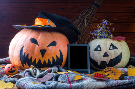 Halloween concept: pumpkins, broom, tablet and autumn leaves on a wooden background, free space. Orange pumpkin in the hat of a witch.の写真素材