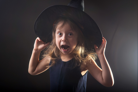 Little girl in witch hat on a dark background, banner for halloween. Portrait of a small sorceress.の写真素材