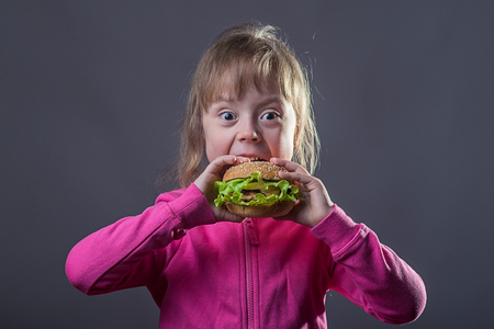Girl eats fast food, portrait on gray background. A child is holding a hamburger, free space.の写真素材