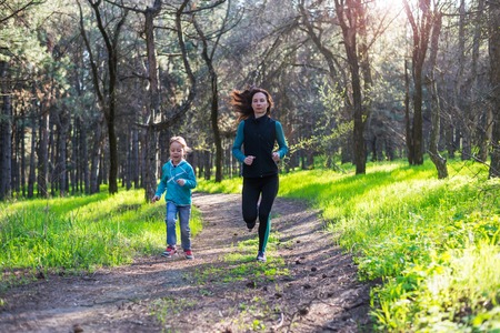 Morning jogging, mom and daughter are running along the forest trail, free space. Active lifestyle.の写真素材