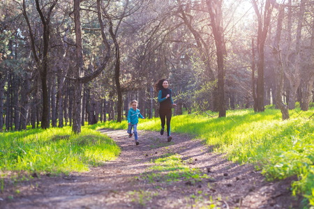 Morning jogging, mom and daughter are running along the forest trail, free space. Active lifestyle.の写真素材