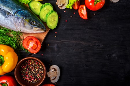 Raw fish and ingredients: lemon, spices, greens, tomato, on a wooden table, top view. Preparation of...