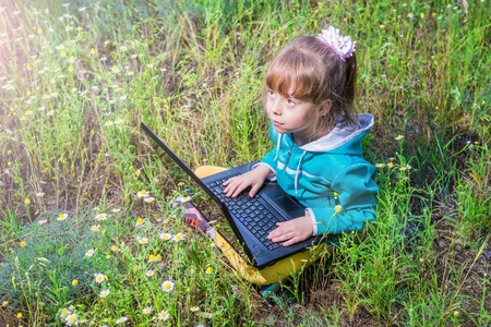 Little girl is sitting with laptop outdoors. Doing homework in the park.の写真素材