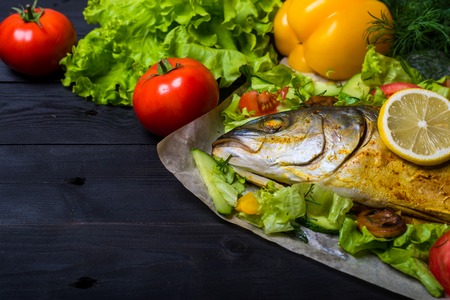 Baked sea fish with vegetables on a wooden table, free space. Grilled tuna.