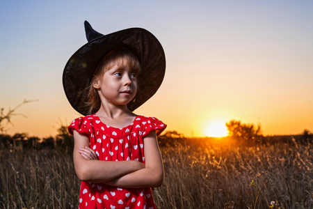 Beautiful little girl in witch costume on sunset background, free space. Background for the holiday of Halloween. Happy Halloween.の写真素材