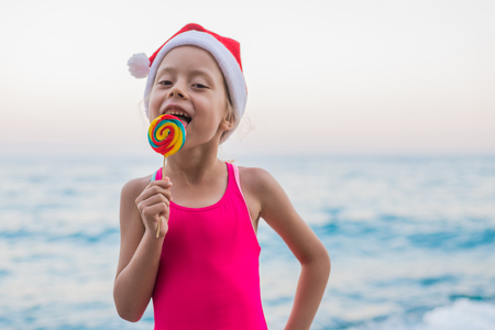 Cute girl celebrating New Year and Christmas on the beach in a hat of Santa Claus, free space. Christmas background, winter holidays in tropical countries.の写真素材