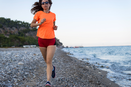 Active lifestyle: a slim woman runs along the beach. Morning run, rear view.の写真素材