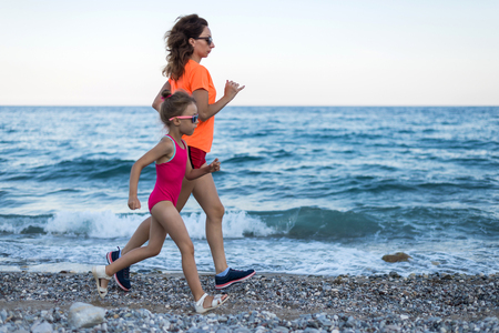 Active lifestyle: mom and daughter run along the beach. Sports family, free space.の写真素材