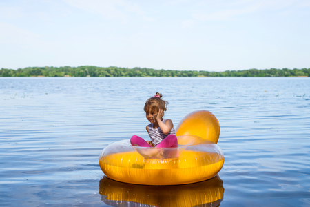 The child is sitting in a rubber ring and talking on a mobile phone. Camping, relaxの写真素材