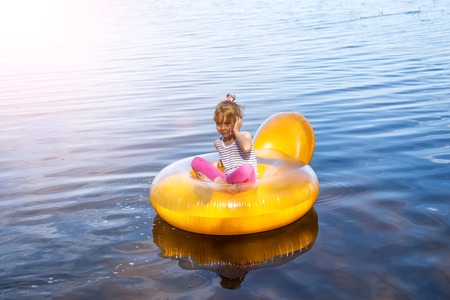 The little girl is resting in an inflatable chair, floating on the water. The child is talking on the smartphone.の写真素材