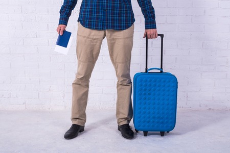 A man with a blue suitcase stands near a white brick wall. Vacation, free space. Businessman at the airport.の写真素材
