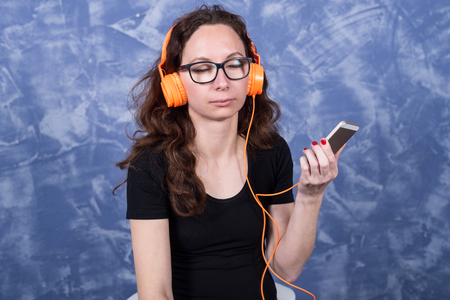 Young woman in glasses listening to music in headphones with the help of a smartphone. Girl in orange headphones with a phone in their hands.の写真素材