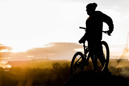 Mountain biker standing on top of a mountain with a bicycle, a beautiful sunset. Silhouette of a cyclist. Copy space.の写真素材