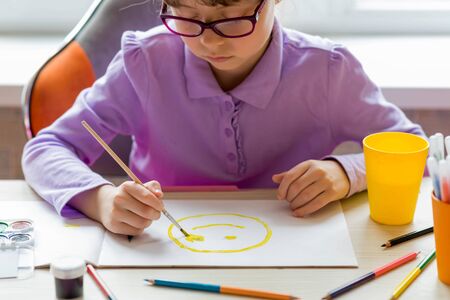 A little schoolgirl sits at a table and paints. The concept of distance learning. Home schooling.の写真素材