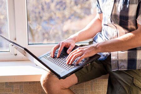Business man working on a laptop while sitting on a windowsill. The concept of remote work. Self...