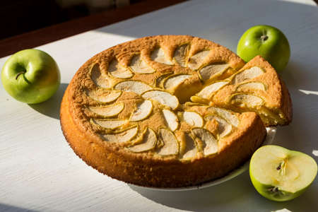 Fragrant apple pie and green apples on a wooden table. Homemade baking.