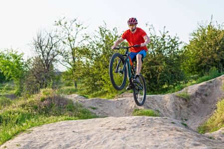 Extreme cycling concept, cyclist jumping on a mountain bike. Cyclist in a bright orange t-shirt and helmet.の写真素材