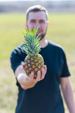 A man holds a pineapple on his outstretched arm. Ripe pineapple.の写真素材