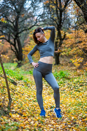 A slender woman in leggings and a crop top poses in the autumn forest. Sports girl.の写真素材