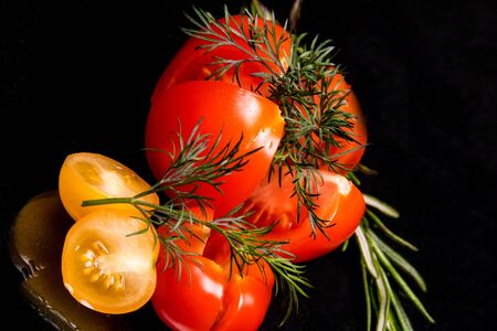 Ripe tomatoes and red yellow cherry with mint basil dill on a black background top viewの写真素材