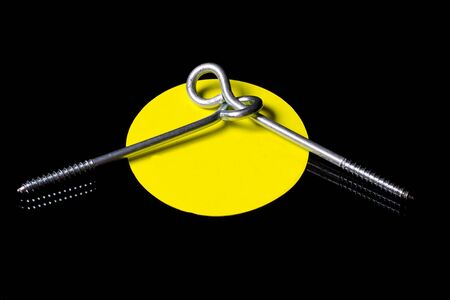Two self-tapping screws with a ring screwed into one another in a yellow circle, with room for text, on a black backgroundの写真素材
