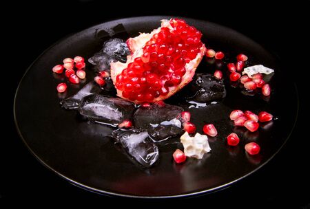 Pomegranate peeled, ice in a black plate on a black background, close-upの写真素材