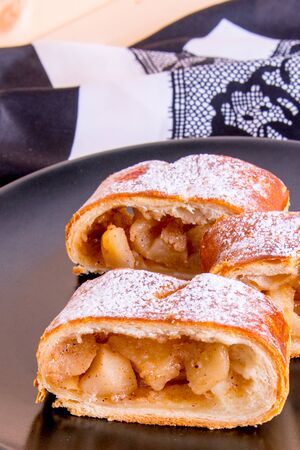 Apple strudel on a black plate with a white napkin on a wooden table, close-up, side viewの写真素材