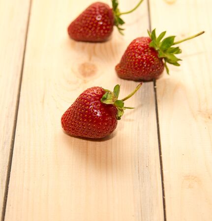 Three strawberries on a wooden table close-upの写真素材