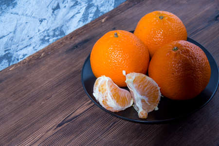 Mandarin slices, Mandarin on a black plate on an old natural wooden table, side view, close-up, space for textの写真素材