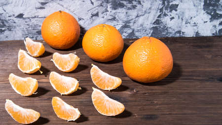 Whole tangerines, slices on a cutting Board, old dark wooden table, close-up with space for text