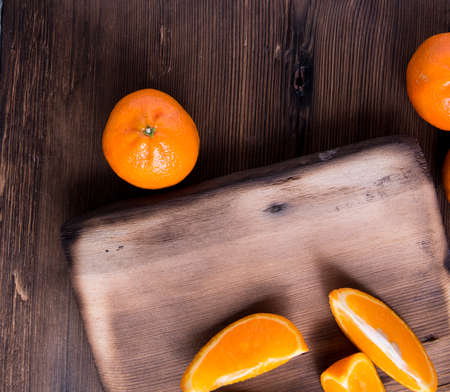 Whole tangerines, slices on a cutting Board, old dark wooden table, close-up with space for tex