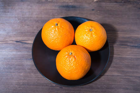 Three tangerines on a black plate, old natural wooden table, top view, close-up, space for textの写真素材
