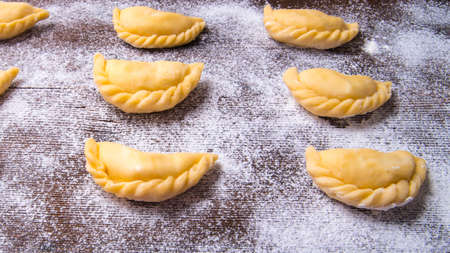 Homemade dumplings, vareniki on an old wooden table, sprinkled with flour, space for text