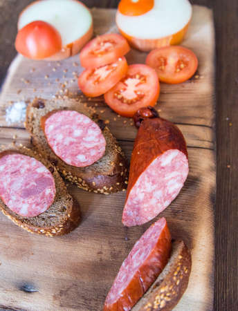 Sausage slices and sandwiches on a wooden Board, with slices of tomatoes, onions with slices of...
