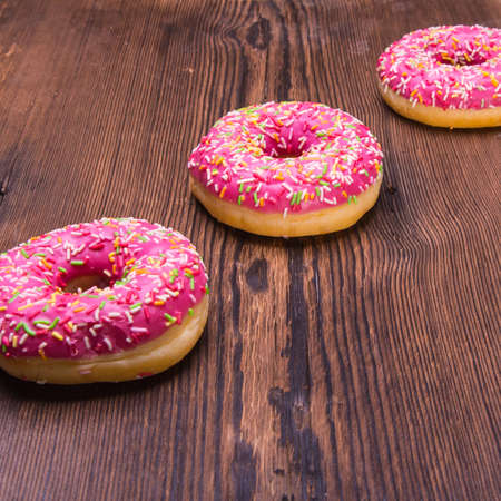 Glazed donuts with pink icing with sprinkles on a wooden Board, space for text, close - upの写真素材