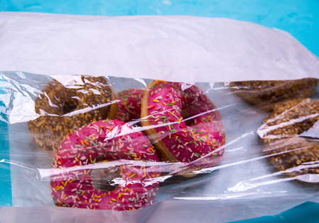 Glazed donuts with pink and chocolate icing with sprinkles in a package in a package on a blue...
