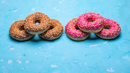 Glazed donuts with pink and chocolate icing with sprinkles on a blue background, space for text,...