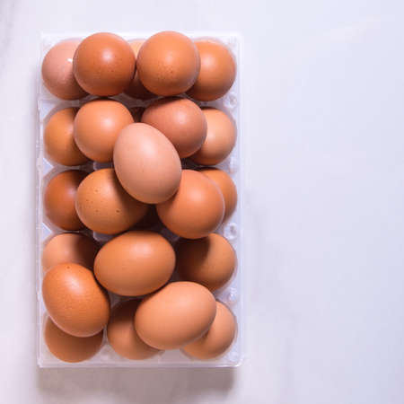 Close-up of fresh brown eggs in a plastic box on a white background, copy spaceの写真素材