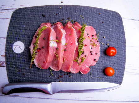Pork. Fresh pork steaks on a black chopping board and spices, cherry tomatoes, rosemary, peppercorns, knife, copy spaceの写真素材