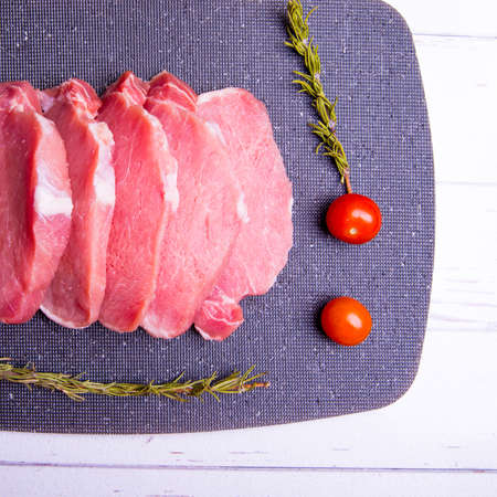 Pork. Fresh pork steaks on a black chopping board and spiced, cherry tomatoes, rosemary,...